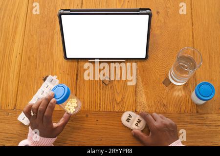 Donna birazziale anziana che effettua videochiamate su tablet con spazio per le copie, che tiene in mano farmaci a casa Foto Stock