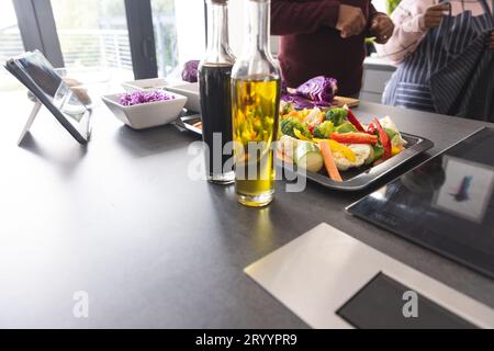 Sezione centrale della coppia birazziale senior che utilizza una compressa per preparare verdure in cucina a casa Foto Stock