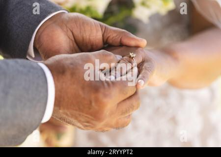 Mani dello sposo birazziale senior che mettono l'anello nuziale al dito della sua sposa Foto Stock