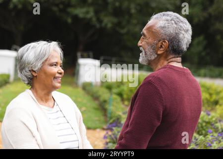 Felice coppia birazziale anziana che si tiene per mano, sorridendo in giardino a casa Foto Stock