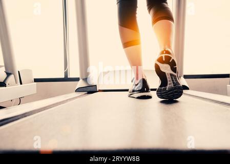 Il corpo inferiore a gambe parte della ragazza di Fitness in esecuzione sulla macchina in esecuzione o il tapis roulant in palestra per il fitness con sun ray. Tono caldo. Una sana e l'attività ginnica Foto Stock