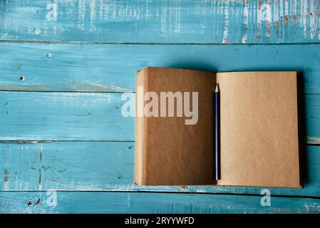 Vista dall'alto del notebook vuoto aperto su sfondo di legno blu con matita viola al centro. Ufficio di cancelleria funzionante. Istruzione e. Foto Stock