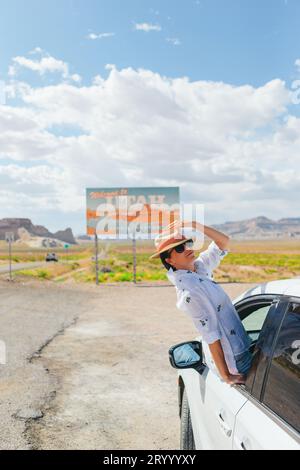 Bella donna nel suo viaggio vicino alla macchina. Benvenuto all'insegna dello Utah Road. Un grande cartello di benvenuto ti dà il benvenuto a Monument Valley, Utah Foto Stock