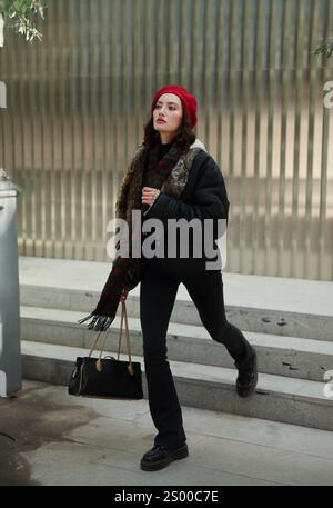 Una giovane donna, vestita con abiti invernali alla moda, cammina con sicurezza attraverso un ambiente urbano vivace Foto Stock