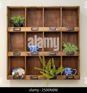 Una parete in legno ospita varie piccole piante in vaso e tazze smaltate. Foto Stock