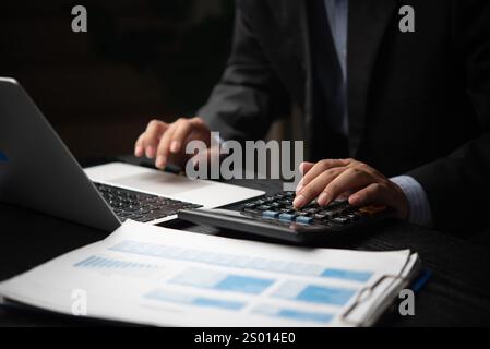 Uomo d'affari che lavora con una calcolatrice e un laptop, analizzando i report finanziari per la definizione del budget e il processo decisionale. Perfetto per la finanza, la contabilità e. Foto Stock