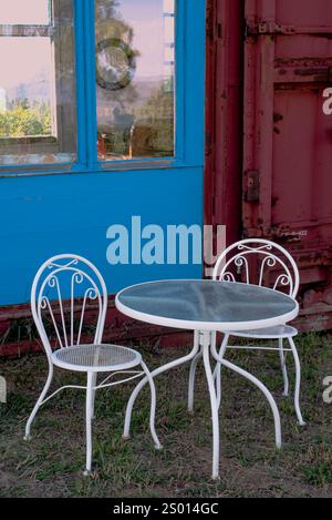 Tavolo da bistrot con tavolo in vetro di fronte al vagone ferroviario rinnovato con pareti in legno color turchese e grandi finestre, New Mexico settentrionale, USA. Foto Stock