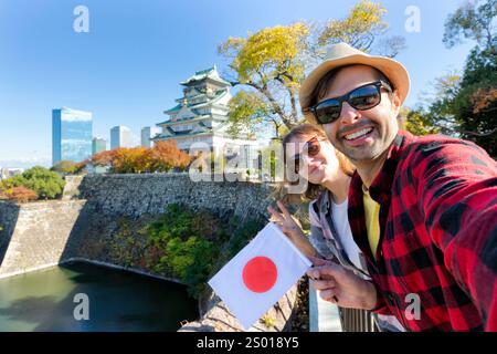 Una giovane coppia di turisti che fa un selfie con la bandiera del Giappone al Castello di Osaka, il Castello di Osaka è uno dei luoghi di interesse più famosi del Giappone e di Osaka, in vacanza Foto Stock