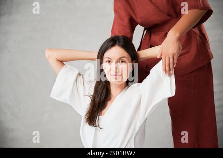 Massaggiatrice che fa un massaggio yoga tailandese. Vista ritagliata della donna terapeuta che esegue un massaggio tradizionale, allungando il corpo della paziente. Primo piano ritratto del cliente che si sta facendo un massaggio alle mani. Foto Stock