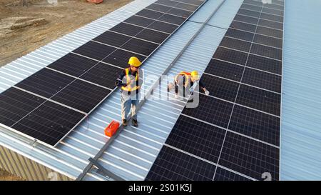 Due lavoratori stanno installando pannelli solari su un tetto in metallo. Uno è accovacciato, fissando i pannelli, mentre l'altro si trova nelle vicinanze, osservando il lavoro. Foto Stock