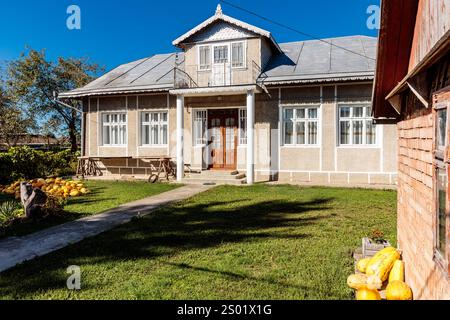 Una grande casa con un tetto bianco e un camino in mattoni rossi. La casa ha un grande portico frontale con un tavolo e sedie. La casa e' circondata da una lussureggiante Foto Stock
