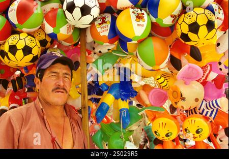 Venditore ambulante di palloncini a Lima, Perù, circondato da coloratissimi giocattoli gonfiabili e palle da spiaggia, che mostrano il vivace commercio locale e la cultura di strada. Foto Stock