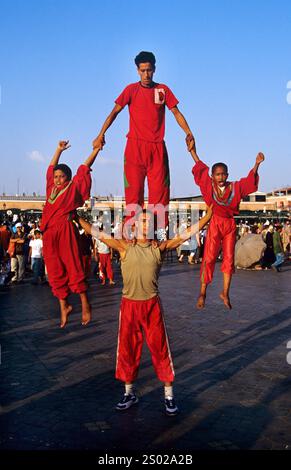 Artisti di strada in vivaci costumi che mostrano abilità acrobatiche a Jemaa el-Fnaa, Marrakech, Marocco, tra una folla vivace e un'atmosfera vivace. Foto Stock