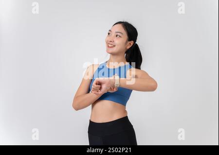Una giovane donna asiatica sorridente in abbigliamento sportivo che controlla le calorie dell'allenamento bruciate sul suo smartwatch. sfondo bianco dello studio. concetti di persone e sport Foto Stock