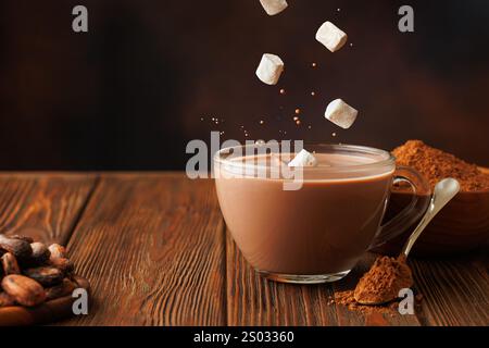 marshmallow che cadono nella cioccolata calda nella tazza di vetro sul tavolo Foto Stock