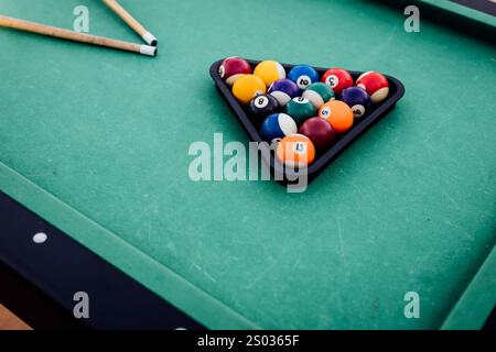 Un tavolo da biliardo con palle da biliardo sparse, un bastoncino e accessori catturati in una scena dinamica e pronta per il gioco. L'attenzione dettagliata sull'apparecchiatura Foto Stock
