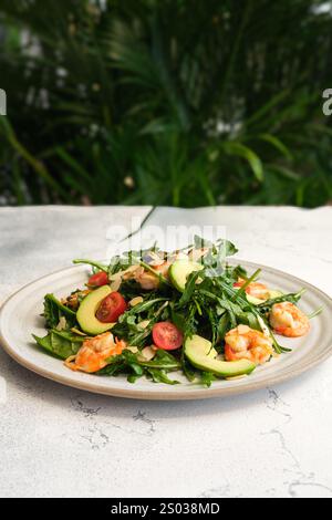 Un'insalata di gamberi freschi con rucola, fette di avocado, pomodori ciliegini e scaglie di mandorle su un piatto di ceramica. Foto Stock