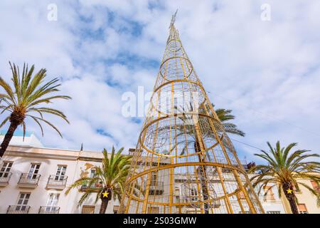 Grande struttura conica in metallo che ricorda la cornice dell'albero di Natale sorge nella piazza della città circondata da palme ed edifici. L'evento festivo combina Foto Stock