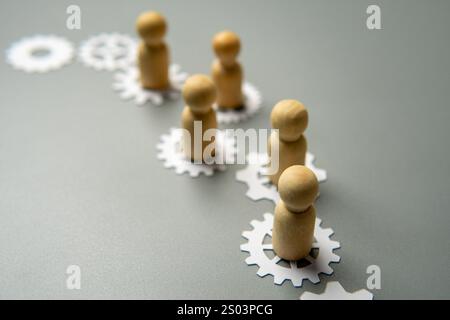 Un'immagine concettuale con figure di legno in piedi su ingranaggi interconnessi. Lavoro di squadra, collaborazione e la natura interconnessa del concetto di lavoro. Foto Stock