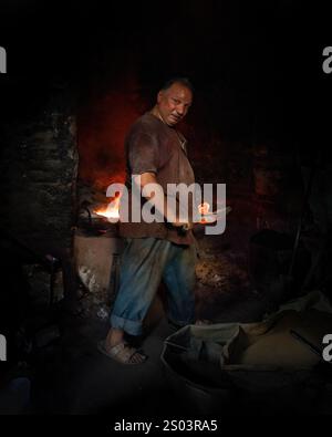 Un operaio di fonderia in un'officina ad Alessandria, Egitto, che fonde metallo fuso in un ambiente tradizionale. Un'immagine del fondatore dell'ottone riflette l'artigianato locale Foto Stock