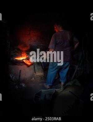 Un operaio di fonderia in un'officina ad Alessandria, Egitto, che fonde metallo fuso in un ambiente tradizionale. Un'immagine del fondatore dell'ottone riflette l'artigianato locale Foto Stock