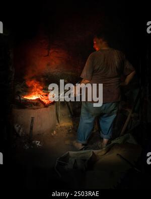 Un operaio di fonderia in un'officina ad Alessandria, Egitto, che fonde metallo fuso in un ambiente tradizionale. Un'immagine del fondatore dell'ottone riflette l'artigianato locale Foto Stock