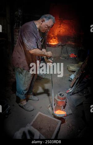 Un operaio di fonderia in un'officina ad Alessandria, Egitto, che fonde metallo fuso in un ambiente tradizionale. Un'immagine del fondatore dell'ottone riflette l'artigianato locale Foto Stock