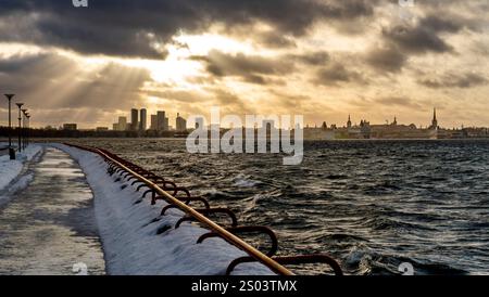 Una vista panoramica di Tallinn durante l'inverno, con una passeggiata sul lungomare. Il cielo è spettacolare con raggi di luce che si infrangono attraverso le nuvole, illuminando Foto Stock