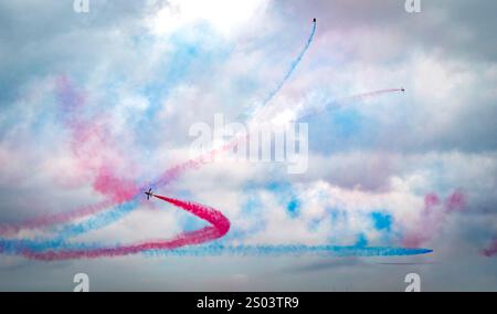 Mostra aerea con aerei che creano colorate piste di fumo nel cielo. Il fumo è di colore rosso e blu, formando schemi dinamici contro una nuvola Foto Stock