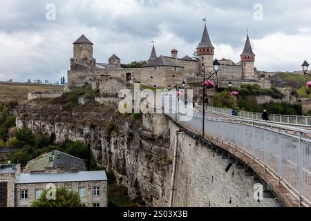 Un gruppo di persone sta camminando su un ponte sopra un muro. Il ponte è in metallo e si trova di fronte a un castello. Il castello è circondato da un Foto Stock