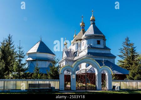 Una grande chiesa bianca con un alto campanile e un piccolo edificio bianco davanti ad esso. La chiesa è circondata da alberi e ha una panchina davanti ad essa Foto Stock