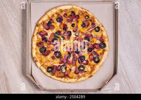 Pizza condita con peperoni, peperoni e olive, confezionata in una scatola di cartone. Foto Stock