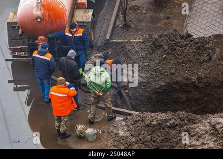 Ucraina, Romny, 24 dicembre 2024: Un gruppo di lavoratori ripara un gasdotto danneggiato in una fossa fangosa con un camion fognario parcheggiato nelle vicinanze. I lavoratori sono S Foto Stock