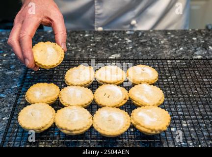 Uomo anziano in bianco chef con mince pie appena sfornate su una griglia rinfrescante per Natale su un bancone da cucina casalingo, Regno Unito Foto Stock