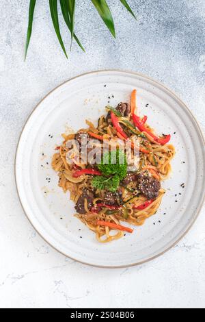 Vista dall'alto dei noodle udon saltati in padella con manzo tenero, peperoni rossi e verdi, fette di zucchine e semi di sesamo. Foto Stock