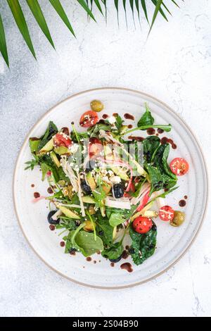 Un'insalata di verdure fresca e colorata con spinaci, pomodori ciliegini, avocado, olive e semi di sesamo, servito su un piatto di ceramica e ricoperto di Foto Stock