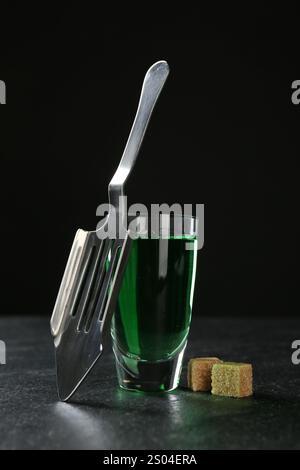 Absinthe nel bicchiere da espresso, zucchero di canna e cucchiaio scanalato sul tavolo su sfondo nero Foto Stock