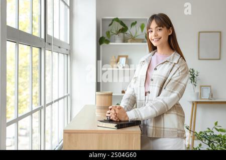 Bella giovane donna con perline di preghiera e Sacra Bibbia in commode a casa Foto Stock