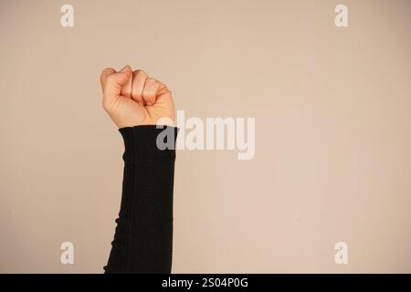 La mano forma un pugno forte, simboleggiando forza e protesta. Questo gesto iconico parla di spirito combattivo. Lo sfondo semplice migliora il powe Foto Stock