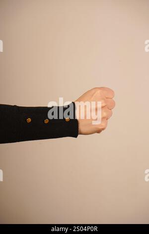 La mano forma un pugno forte, simboleggiando forza e protesta. Questo gesto iconico parla di spirito combattivo. Lo sfondo semplice migliora il powe Foto Stock