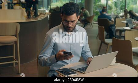 Uomo d'affari indiano Guy uomo d'affari arabo utente maschio visitatore in caffetteria speranza desiderio tenere telefono cellulare ricevere cattive notizie messaggio truffa guasto cellulare Foto Stock