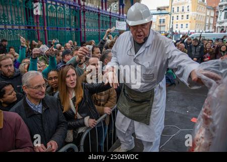 Un macellaio tiene la mano di una donna per passarle un pezzo di carne. In una tradizione che ha più di un secolo, i commercianti di Smithfield mercatino tengono l'annuale asta di carne di Natale. Poiché il mercato della carne vecchio di 900 anni chiude per le festività natalizie, i prodotti in eccedenza vengono venduti al pubblico a un prezzo ridotto. La folla si riunisce dalle prime ore del mattino della vigilia di Natale per rivendicare il posto migliore nella Grand Avenue, in posizione centrale nel mezzo del mercato. Macellai e facchini sfilano tagli di carne davanti al pubblico in attesa che vengono rapidamente scambiati in contanti Foto Stock