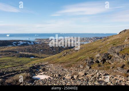 Questa immagine mozzafiato cattura la vista estiva di Qeqertarsuaq, situata sull'isola di Disko, in Groenlandia, da una montagna vicina. Il villaggio si vede nido Foto Stock