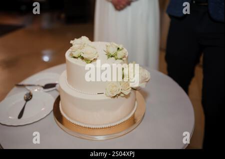 Elegante torta bianca nuziale adornata con rose fresche. Foto Stock