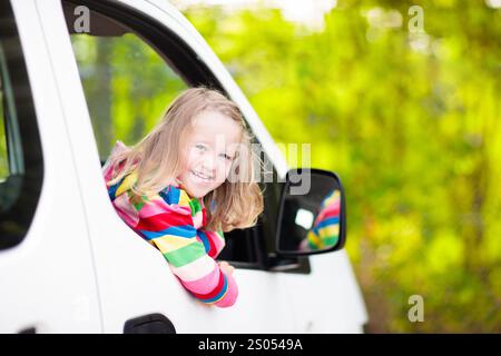 Bambina che guarda fuori dal finestrino dell'auto durante una vacanza in famiglia in viaggio in auto il giorno d'estate. Viaggia con un bambino. Bambino in minivan bianco. Viaggiando in auto Foto Stock