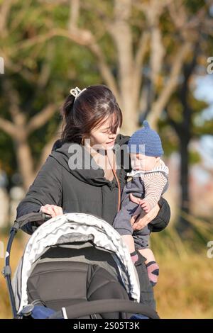 Una donna di 30 anni che indossa un piumino che spinge un passeggino con il suo bambino giapponese di 5 mesi trascorre una fredda serata invernale in un parco di Hakata City, Foto Stock