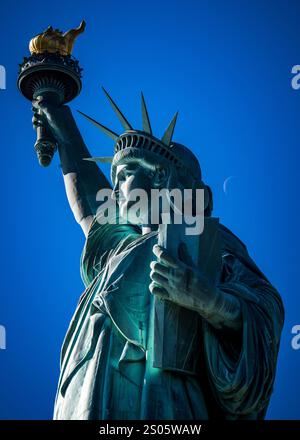 La Statua della libertà sorge su Liberty Island, un faro di libertà e speranza. Splendida luce che cattura la sua maestosità sullo sfondo del cielo blu. Foto Stock