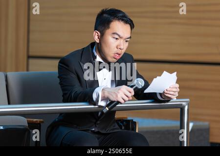 Un giovane studente universitario è a un concorso di lingua pubblica, seduto in una sala auditorium, leggendo le sue schede di scrittura e preparandosi mentre attende Foto Stock