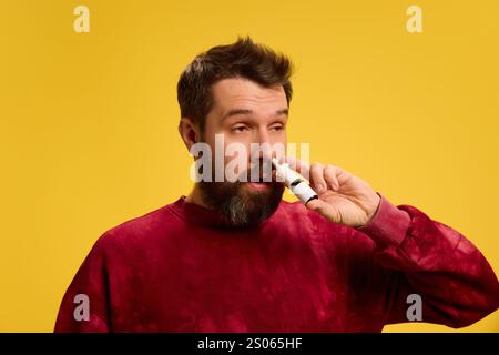 Il giovane con il naso che cola, soffre di allergia, spruzzandolo per rimuovere i sintomi sullo sfondo giallo dello studio. Foto Stock