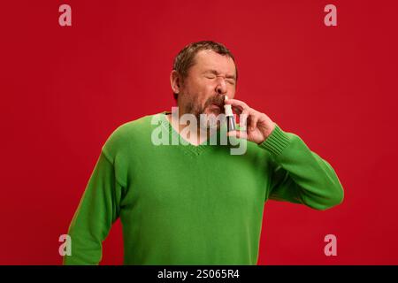 Uomo che spruzza farmaci nasali, occhi schiacciati chiusi, che mostrano sintomi di congestione nasale o sinusite causata da malattia. Foto Stock